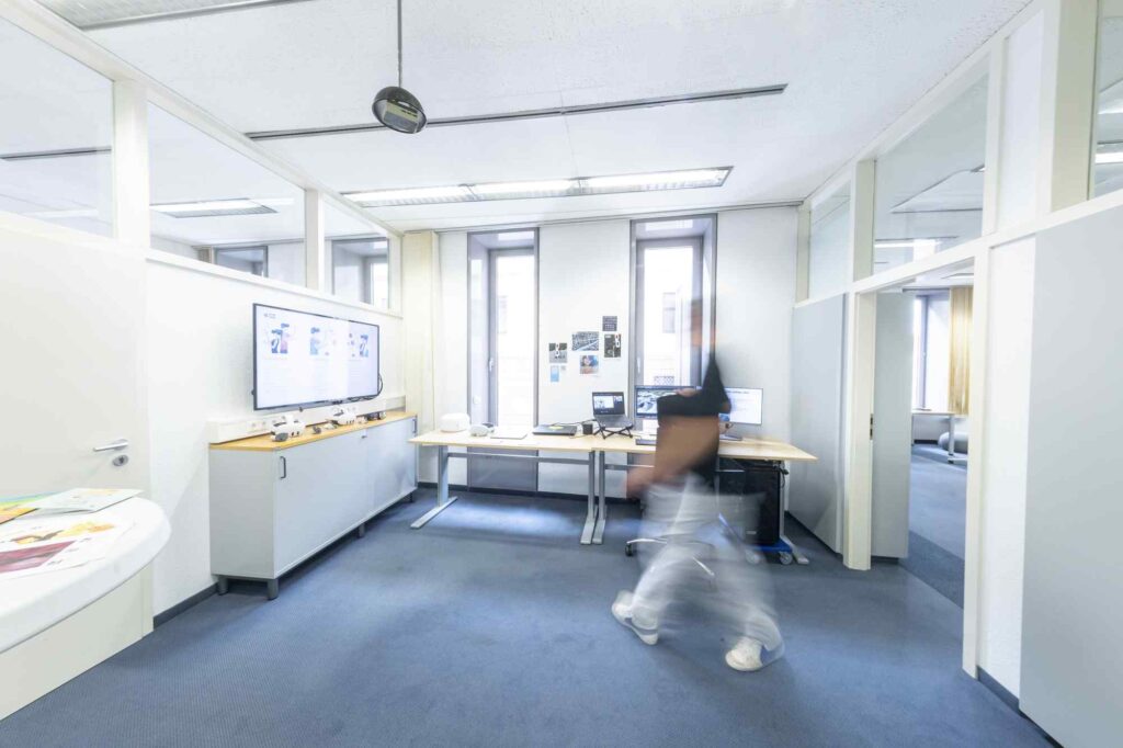 Moderner Besprechungsraum im Digitalisierungszentrum mit Monitor und unscharfer Person im Vordergrund.