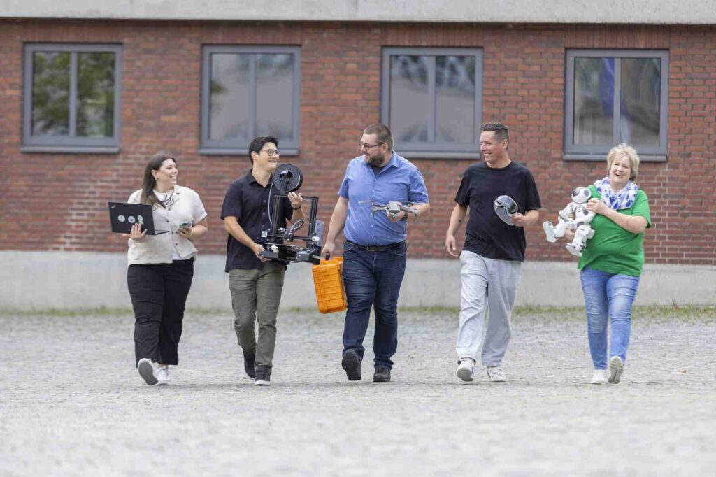 Eine Gruppe von Menschen geht zusammen vor einem Backsteingebaeude.