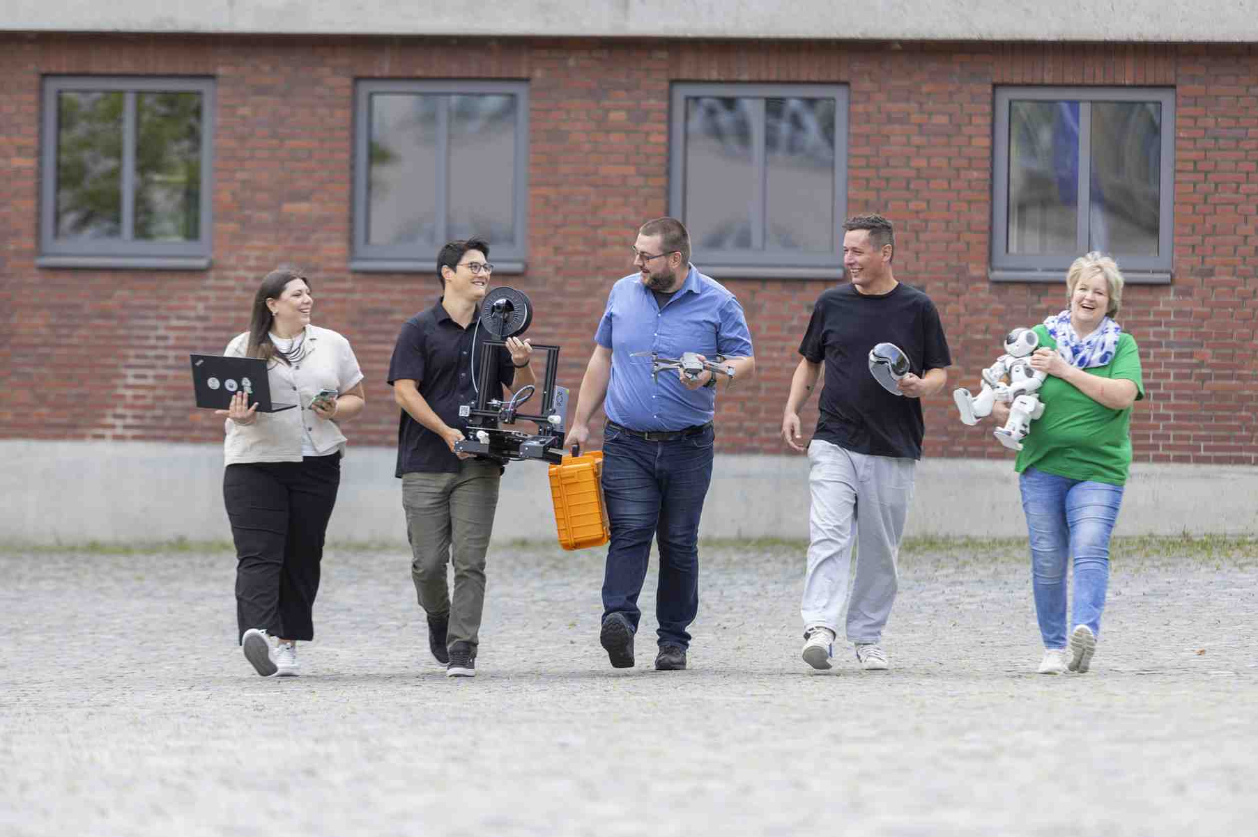 Eine Gruppe von Menschen geht zusammen vor einem Backsteingebaeude.