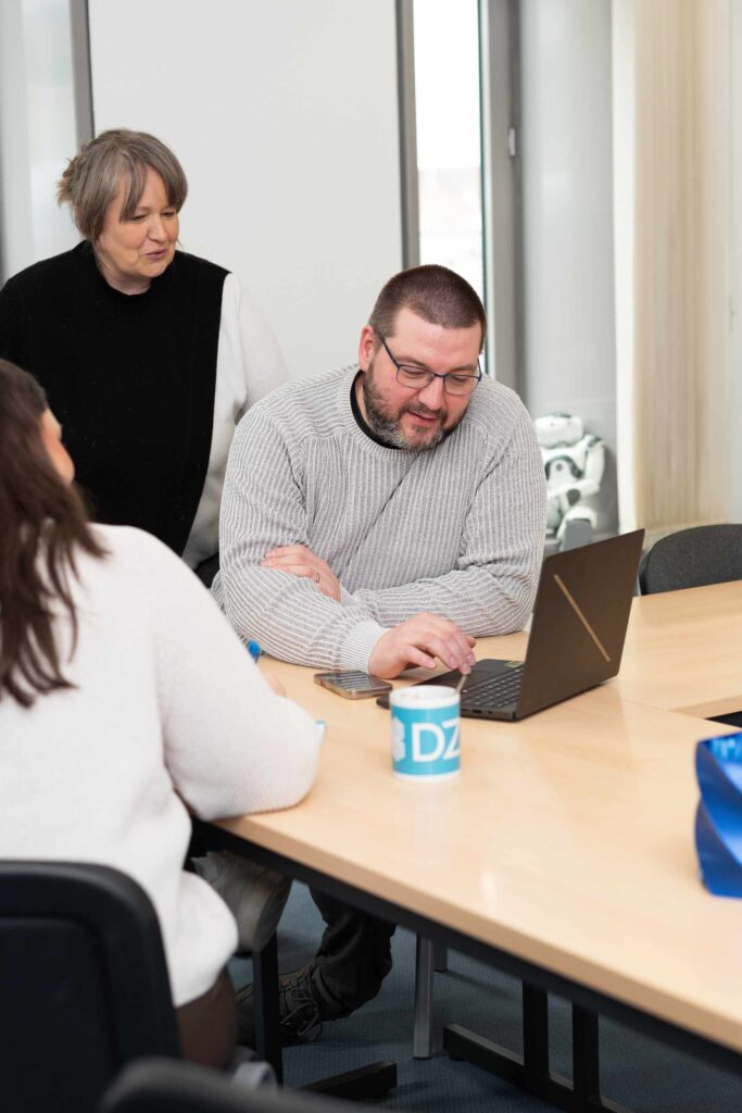 Mitarbeiter bei einer Besprechung im Digitalisierungszentrum, sitzend am Tisch mit Laptop.