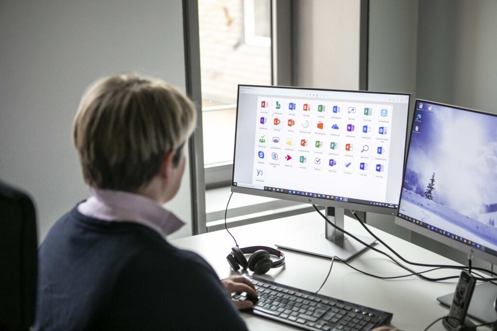 Schulterblick auf einen Bildschirm, auf welchem Office Anwendungen zu sehen sind.