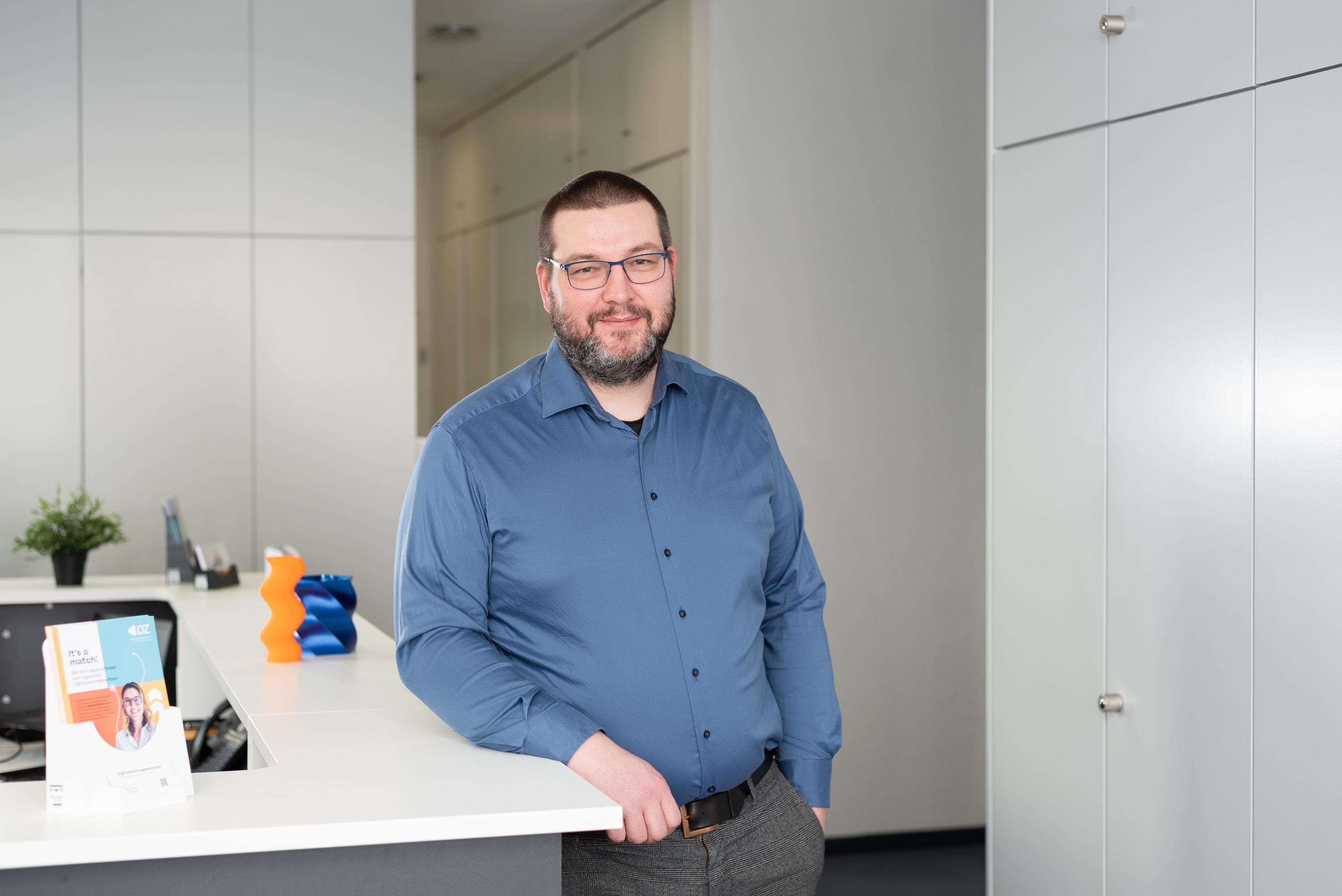Alexander Nikolaus steht am Empfang eines modernen Bueros im Digitalisierungszentrum Ulm Alb-Donau Biberach Neu-Ulm.
