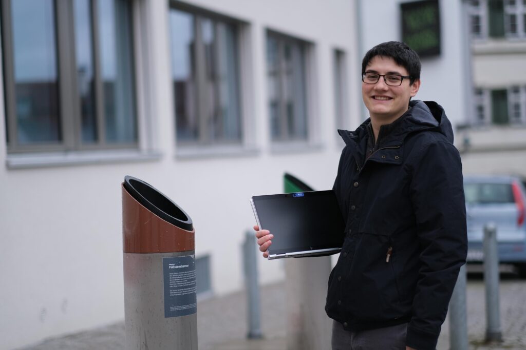 Mann mit Laptop steht in der Fußgängerzone.