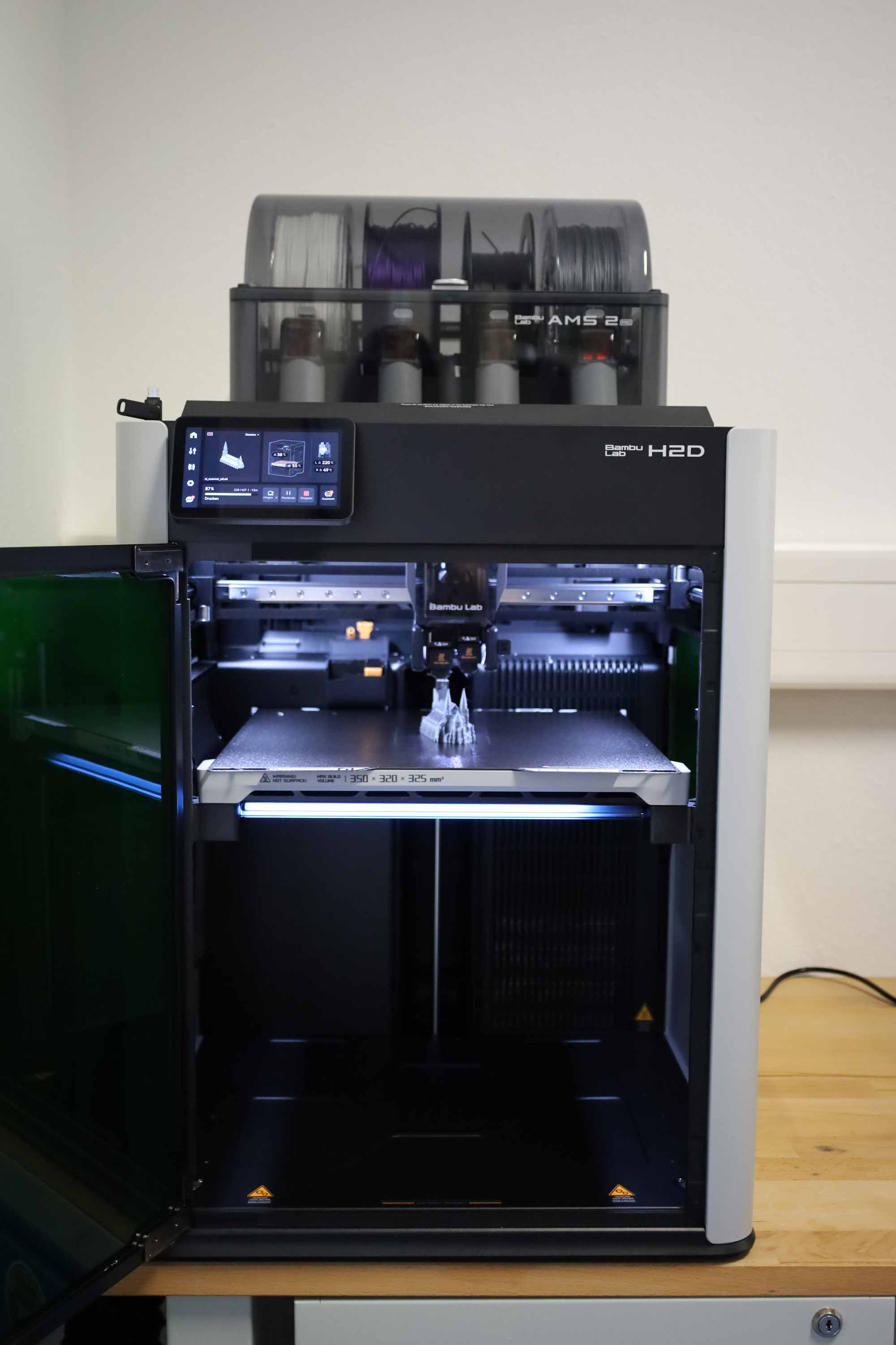 Geoeffneter 3D Drucker fertigt ein kleines Modell und wird ueber mehrere Filamentrollen mit Material versorgt.