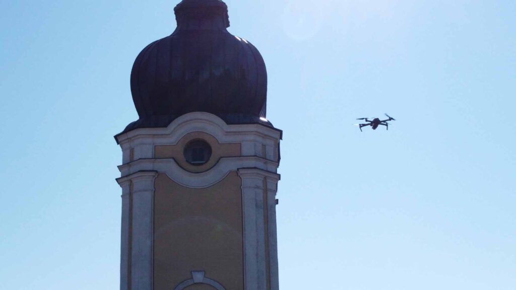 Drohne fliegt neben dem Turm einer Kirche vor blauem Himmel.
