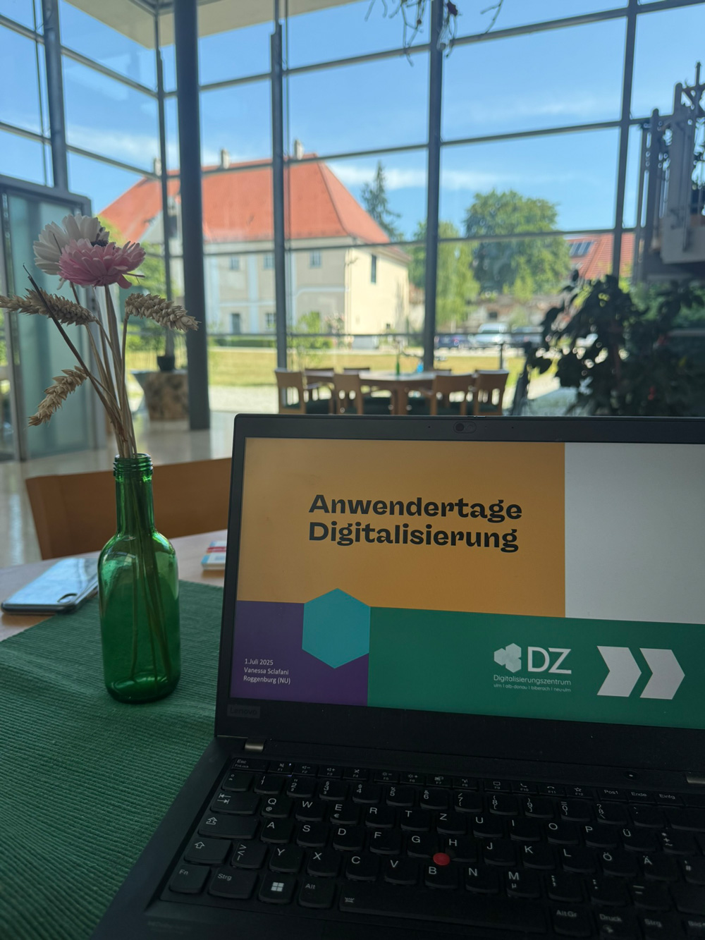 Laptop mit Praesentation der Anwendertage Digitalisierung auf einem Tisch vor einer grossen Glasfassade.