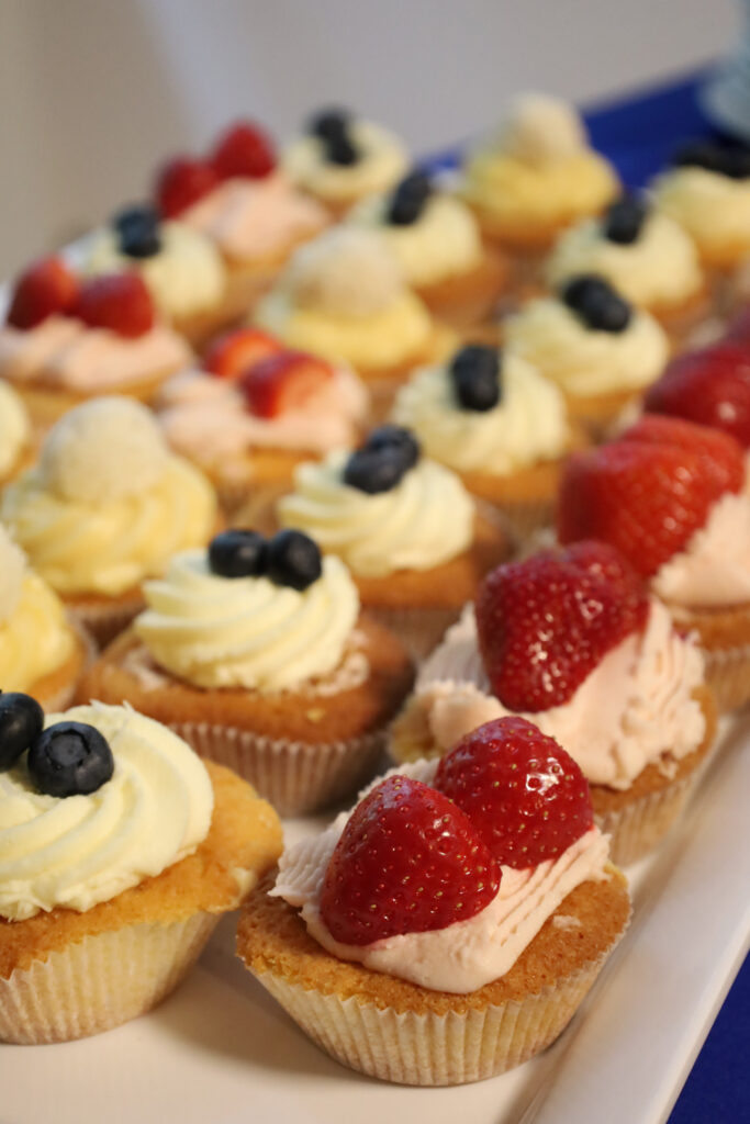 Cupcakes mit heller Creme sowie frischen Erdbeeren und Heidelbeeren auf einer Platte.