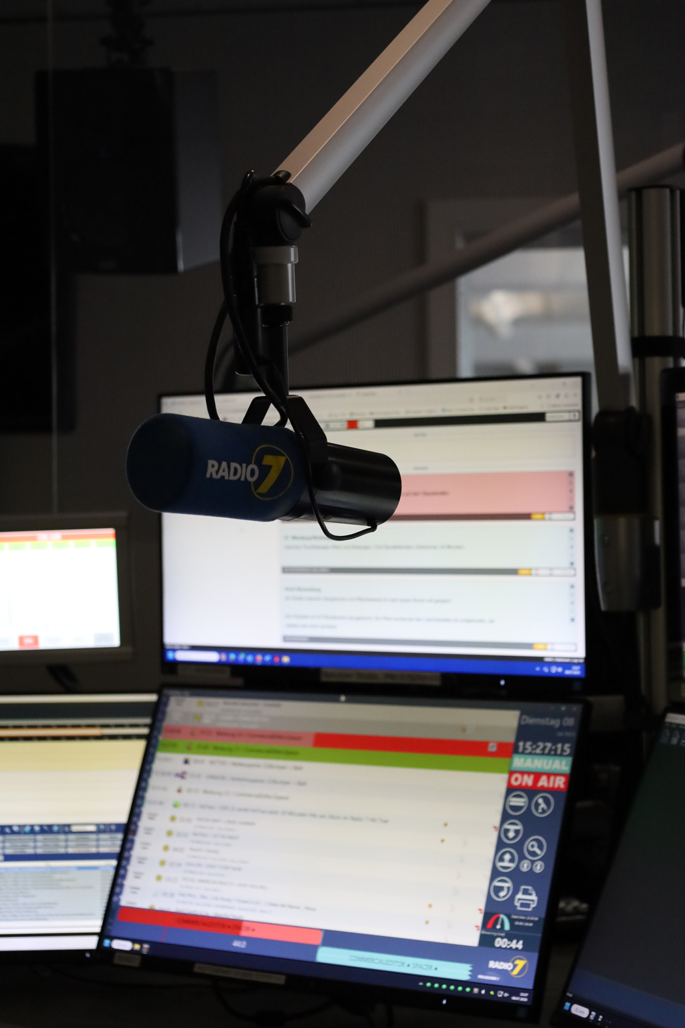 Radio 7 Mikrofon vor mehreren Monitoren mit Sendesoftware und On Air Anzeige im Radiostudio.