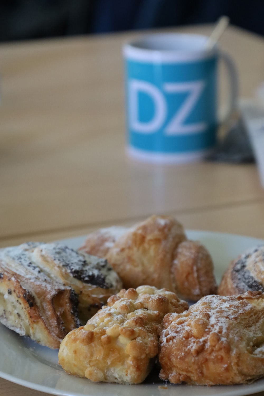 Ein Teller mit verschiedenen Gebaeckstuecken steht vor einer blauen Tasse mit der Aufschrift DZ.