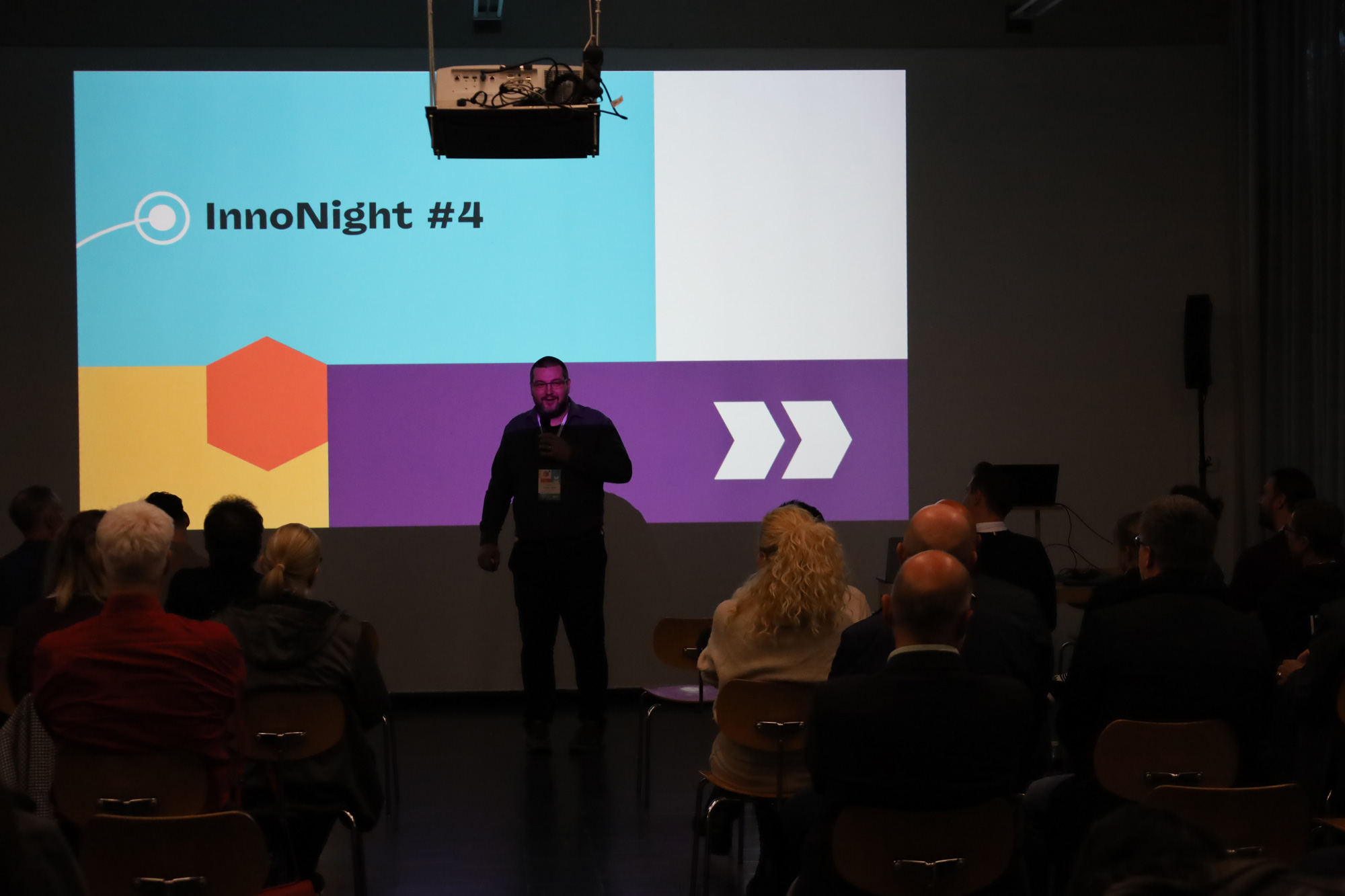 Praesentation vor Publikum bei der Veranstaltung InnoNight 4 mit projiziertem Veranstaltungstitel im Hintergrund.