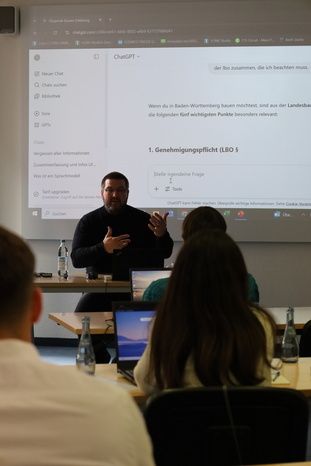 Vortragender praesentiert ChatGPT zum Thema Landesbauordnung vor Teilnehmenden mit Laptops.