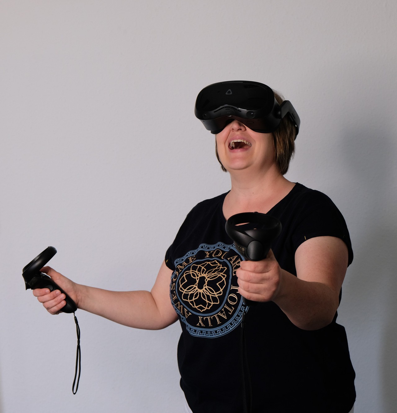 Lachende Person mit Virtual Reality Brille und zwei Controllern in den Haenden.