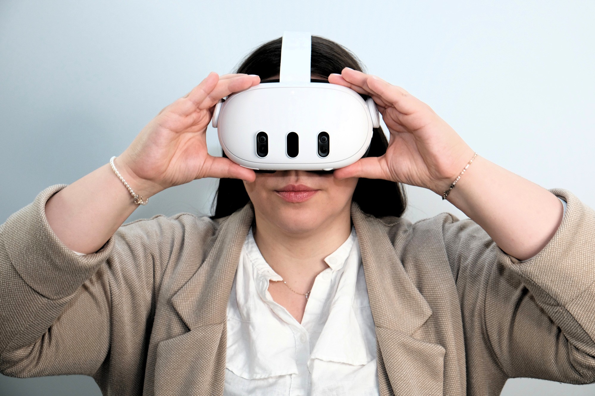 Frau traegt eine weisse VR Brille und haelt sie mit beiden Haenden am Kopf.